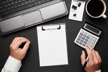 Top view of businessman's hands working. Modern black office desk with laptop, notebook, pencil and a lot of things. Flat lay table layout. Copy space for text.