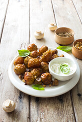 Fried little potatoes and mushrooms on white plate on natural wooden background