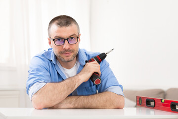 Man Holding Electric Drill Sitting Looking At Camera At Home