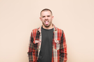 young handsome man feeling disgusted and irritated, sticking tongue out, disliking something nasty...