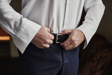 Businessman putting on a belt, fashion and clothing concept,groom getting ready in the morning before ceremony