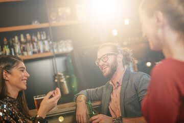 Group of cheerful friends standing near bar counter, drinking beer and chatting.
