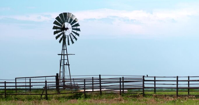 short windmill turning in strong breeze above a cattle corral on prairie summer afternoon