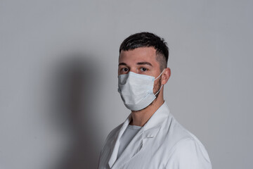 portrait of a brunette male nurse in a white coat with a mask on his face on a white background