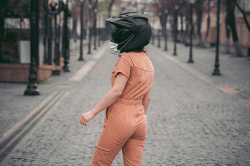 slender girl in overalls. woman is standing in a motorcycle helmet with a medical mask. Photo without  face. Against the background of the street and road. coronavirus, infection, quarantine, covid-19