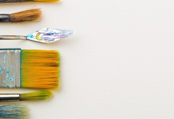 Artistic art supply utensils with brushes on white canvas background with copy space flat lay top...