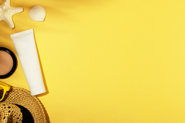 Summer vacation background with accessories. Straw hat, shell, starfish and sunglasses. Unbranded tube for for sunscreen or moisturizing lotion, cosmetics products. Copy space on yellow backdrop