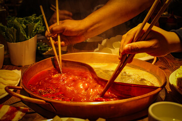 Unrecognized arms taking food with chinese sticks from boiling soup