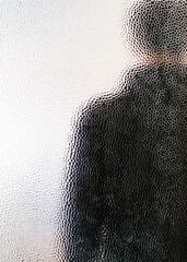 Man in black hoodie behind closed door seen through glass.