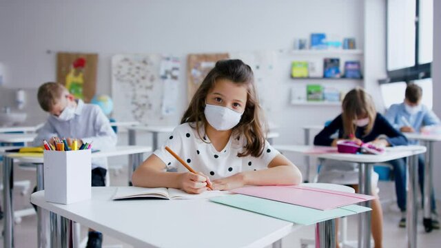 Child with face mask back at school after covid-19 quarantine and lockdown, writing.
