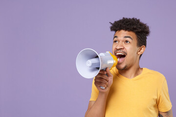 Shocked young african american guy in casual yellow t-shirt posing isolated on violet wall background studio portrait. People lifestyle concept. Mock up copy space. Scream in megaphone, looking aside.