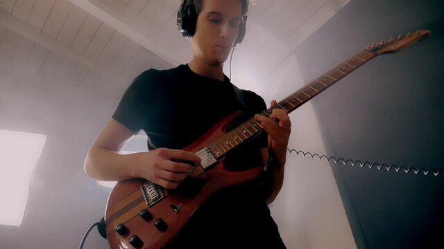 Low angle young male guitarist wearing headphones playing on electric guitar at studio