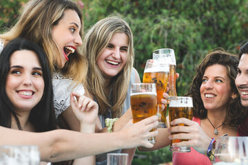 Group of happy friends celebrating and toasting with beer at a bar in summer