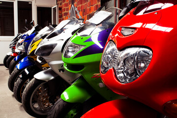 Fototapeta premium Colored sports, road beautiful bikes in a motor show, close up. Many motorcycles parked in a store. Sale of used cruise motorbikes in the cabin. Showroom equipment in the garage.