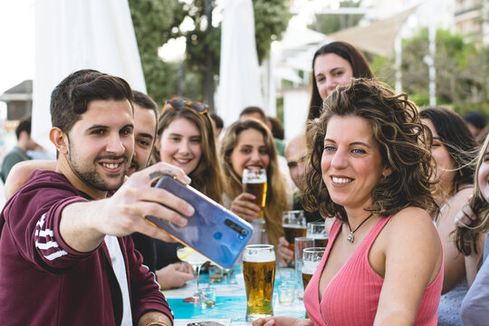 Group of male and female friends taking a photo at a bar while drinking beer