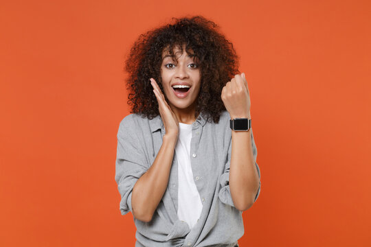 Excited young african american woman in gray casual clothes isolated on orange background studio portrait. People lifestyle concept. Mock up copy space. Wearing smart watch on hand put hand on cheek. - Powered by Adobe