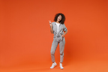 Fototapeta na wymiar Cheerful young african american woman girl in gray casual clothes posing isolated on orange background studio portrait. People emotions lifestyle concept. Mock up copy space. Showing victory sign.