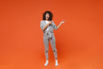 Excited young african american woman girl in gray casual clothes posing isolated on orange background studio portrait. People emotions lifestyle concept. Mock up copy space. Point index fingers aside.