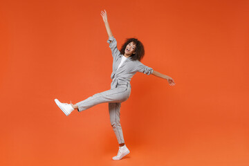 Cheerful young african american woman girl in gray casual clothes posing isolated on orange background studio. People lifestyle concept. Mock up copy space. Spreading rising hands and legs having fun.