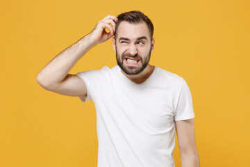 Fototapeta na wymiar Preoccupied young bearded man guy 20s in white casual t-shirt posing isolated on yellow wall background studio portrait. People lifestyle concept. Mock up copy space. Put hand on head, looking aside.