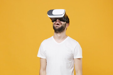 Cheerful young bearded man guy in white casual t-shirt posing isolated on yellow wall background studio portrait. People sincere emotions lifestyle concept. Mock up copy space. Watching in headset.