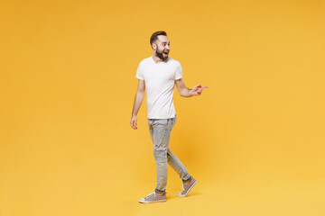 Excited young bearded man guy in white casual t-shirt posing isolated on yellow background studio portrait. People sincere emotions lifestyle concept. Mock up copy space. Pointing index finger aside.