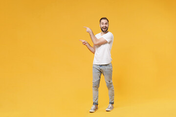 Fototapeta na wymiar Excited young bearded man guy in white casual t-shirt posing isolated on yellow background studio portrait. People sincere emotions lifestyle concept. Mock up copy space. Pointing index fingers aside.