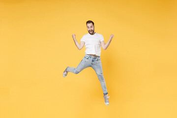 Fototapeta na wymiar Excited young bearded man guy in white casual t-shirt posing isolated on yellow background studio portrait. People emotions lifestyle concept. Mock up copy space. Jumping clenching fists like winner.