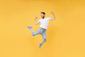 Fototapeta na wymiar Happy young bearded man guy in white casual t-shirt posing isolated on yellow background studio portrait. People emotions lifestyle concept. Mock up copy space. Jumping clenching fists like winner.