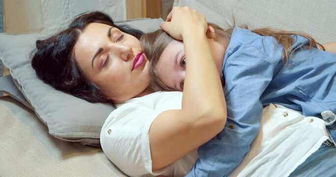 Caring mother hugging and caressing her little daughter lying on the sofa at home. Motherhood concept.