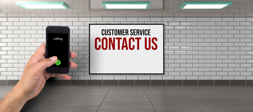 hand holding smartphone ready to call in front of a billboard with the text CUSTOMER SERVICE - CONTACT US