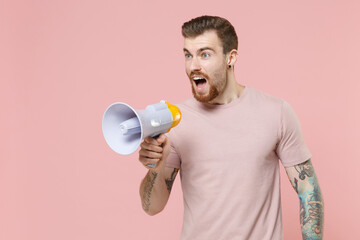Shocked young bearded tattooed man guy in pastel casual t-shirt posing isolated on pink background studio portrait. People lifestyle concept. Mock up copy space. Scream in megaphone, looking aside.