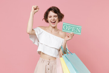 Happy young woman girl in summer clothes isolated on pink background. Shopping discount sale concept. Mock up copy space. Hold package bag with purchases, sign with OPEN title, doing winner gesture.