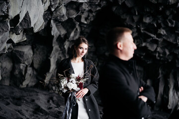 Destination Iceland wedding. Wedding couple under a rock of basalt stones. Bride and groom on the black beach of Vik.