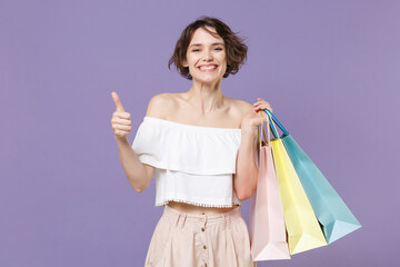 Smiling young woman girl in summer clothes hold package bag with purchases isolated on pastel violet background studio portrait. Shopping discount sale concept. Mock up copy space. Showing thumb up.