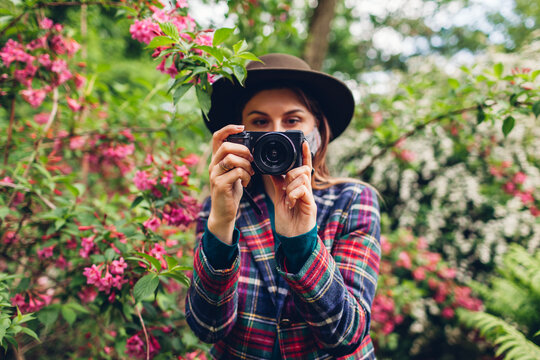 Woman photographer shooting pictures on digital camera in summer garden wearing protective mask. Freelancer walking