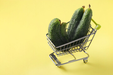 Grocery trolley with two ugly cucumbers on bright yellow background. Concept environmental...
