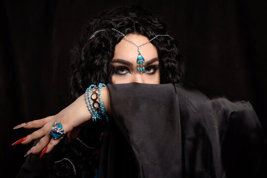 Portrait of an Oriental girl with bright make-up in blue dress and black veil with turquoise jewelry on a dark background.