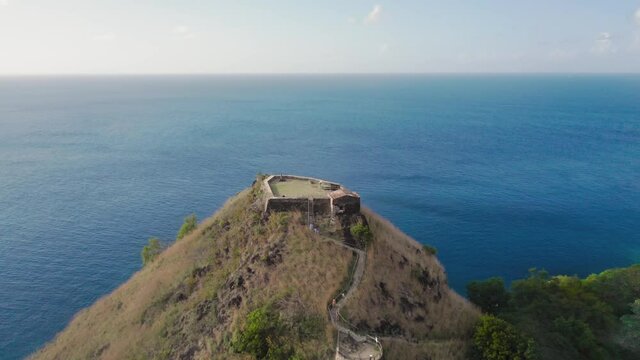 Aerial drone approaching Fort Rodney on top of a mountain in a blue sea at Rodney Bay, Saint Lucia