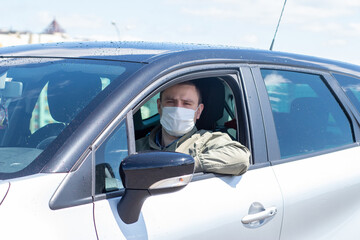 Protect yourself from the coronavirus with a mask while driving. A masked driver in a silver car