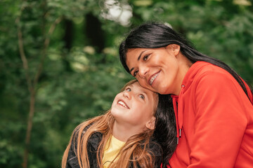 Fototapeta premium Beautiful mother and her cute daughter are hugging and enjoying together while spending a good time in nature.