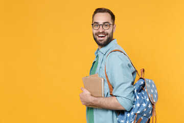 Fototapeta premium Side view of funny man student in casual clothes glasses backpack hold books isolated on yellow background. Education in high school university college concept. Mock up copy space. Looking camera.