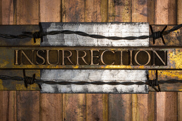 Photo of real authentic typeset letters forming Insurrection text with barbed wire on vintage textured silver grunge copper and gold background