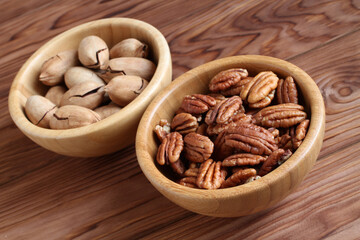 Peeled pecan nuts and unpeeled pecan nuts in bamboo bowls on wooden background