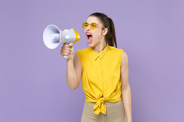 Angry young brunette woman girl in yellow casual shirt posing isolated on violet wall background studio portrait. People sincere emotions lifestyle concept. Mock up copy space. Screaming in megaphone.