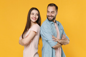 Smiling young couple friends guy girl in casual clothes isolated on yellow background. People lifestyle concept. Mock up copy space. Standing back to back holding hands crossed, looking at each other.