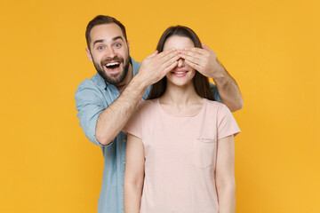 Fototapeta premium Excited young couple two friends guy girl in pastel blue casual clothes posing isolated on yellow background studio portrait. People lifestyle concept. Mock up copy space. Covering eyes with hands.