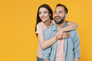 Fototapeta premium Cheerful young couple two friends guy girl in pastel blue casual clothes isolated on yellow background studio portrait. People emotions lifestyle concept. Mock up copy space. Hugging, looking aside.