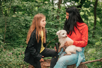 Happy mother and her daughter chatting and playing with dog outdoors.