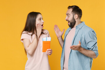 Shocked young couple friends guy girl isolated on yellow background. Passenger traveling abroad to travel on weekends getaway. Air flight journey concept. Hold passport tickets, looking at each other.